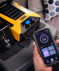 Professional 2000 Watt Power Inverter For Cars And Trucks Featuring Bluetooth Remote And Fast Charge Usb C Ports To Keep Your Devices Juiced Up Without Breaking A Sweat On Long Drives next to a smartphone displaying output power.
