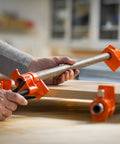 PONY pipe clamp fixtures, orange, 2-pack for 3/4-inch black pipe, side view securing a wooden board.