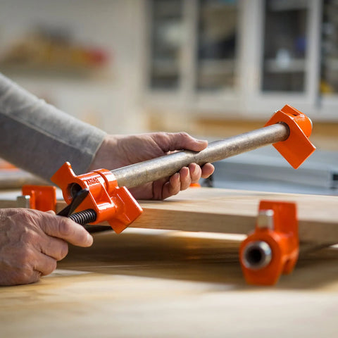 PONY pipe clamp fixtures, orange, 2-pack for 3/4-inch black pipe, side view securing a wooden board.