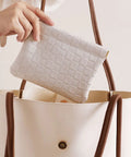 Hand reaching for a leather cosmetic pouch for purse with secure snap closure and slim profile inside a handbag.
