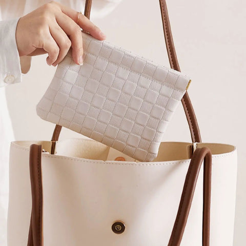 Hand reaching for a leather cosmetic pouch for purse with secure snap closure and slim profile inside a handbag.