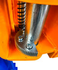 Two-post car lift close-up showing metal gear rack, coil spring, and chrome piston inside orange frame.
