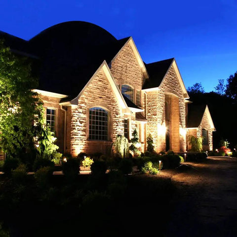 JUDYSSY Outdoor Solar Flood Lights illuminating a stone house and garden at night, showcasing security lighting and landscaping.
