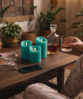 Turquoise Real Wax Flameless Candles Set Of 3 on coffee table with remote, glass of whiskey, and magazines in cozy living room.
