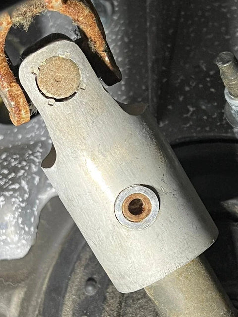 Installed silver aluminum steering column intermediate shaft sleeve with rusted clamp and visible bore.