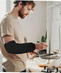 Six Pairs Oil Resistant Arm Sleeves Long Kitchen Cooking Oversleeves With Grippy Elastic Bands Keeping Your Clothes Clean During The Daily Hustle worn by a man cooking pancakes in a kitchen.