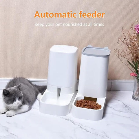 Automatic pet feeder with food and water next to a gray and white cat on a tiled floor.