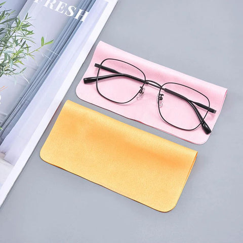 Two microfiber eyeglass cleaning cloths, pink and yellow, with a pair of glasses on the pink cloth.