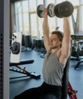 Gym Ready Magnetic Phone Holder With Alloy Base And Ball Joint Attaches To Metal Surfaces Dual Magnetic Mount For MagSafe iPhone 12 13 14 15 16 17 And Android With Metal Ring Secure Grip installed on gym equipment with person exercising in background.
