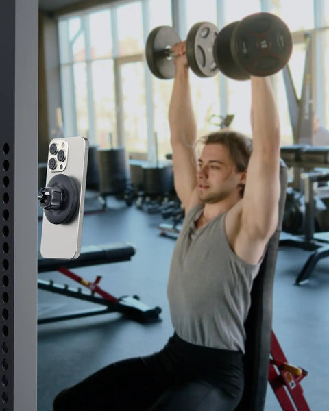 Gym Ready Magnetic Phone Holder With Alloy Base And Ball Joint Attaches To Metal Surfaces Dual Magnetic Mount For MagSafe iPhone 12 13 14 15 16 17 And Android With Metal Ring Secure Grip installed on gym equipment with person exercising in background.