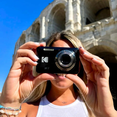 A Real Deal 16 Megapixel Digital Camera With 5X Optical Zoom being held up for a selfie in front of a historic building.