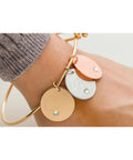 Gold-tone bracelet with three circular disk charms in rose and silver tones and crystals on the wrist (front view).