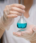 Person holding a flask with blue liquid, wearing Straight Up Premium Clear Vinyl Exam Gloves Large 1000 Pack Latex Free Powder Free.