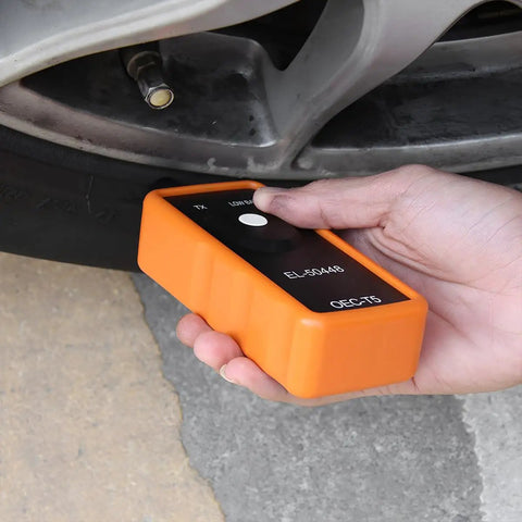 Tire Pressure Monitor System Relearn Tool El-50448 Orange Grip Battery Powered Sensor Reset Kit For Gm Vehicles in hand near tire valve.