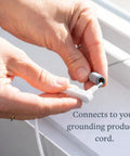 Close-up of hands attaching a white grounding cord plug to a gray earthing stake adapter.