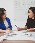 Two women at a meeting with Clear Acrylic Desk Name Plates 2 By 8 Inch Name Tents Pack Of 60 For Classroom Office Meetings.