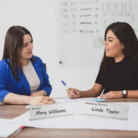 Two women at a meeting with Clear Acrylic Desk Name Plates 2 By 8 Inch Name Tents Pack Of 60 For Classroom Office Meetings.