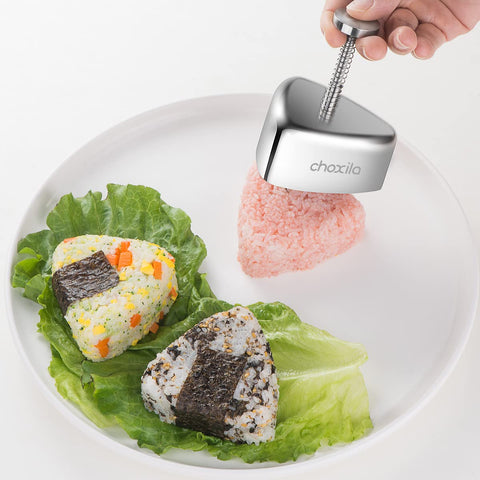 Choxila stainless steel onigiri mold with spring press; two triangular rice balls on lettuce, one wrapped in nori.