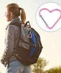 Woman with backpack using 10 Pack Heart Shaped Carabiners With Star Design, colorful clip detail displayed, outdoor scene.