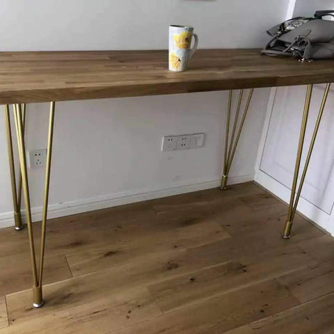 Heavy Duty 28 Inch Gold Hairpin Table Legs With Adjustable Leveling Bolts holding a wooden tabletop and a cup.