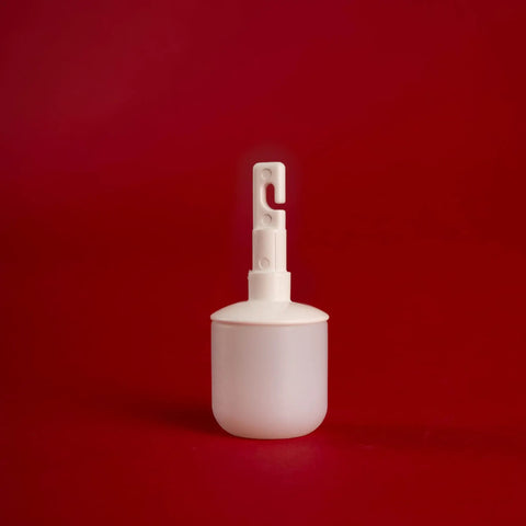 White plastic object with a small hook on top, standing on a red background.
