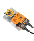 Industrial Grade Damper Actuator With No Sweat Setup And Smooth Operation For 24 Volt Ac Dc Systems Featuring Rock Solid 20 Nm Torque Control And Built Tough Reliability. Orange actuator with silver bracket on a light metal frame.