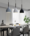 Modern dining room with pendant lights above a long table, showcasing seating for eight and a decorative plant near the window.