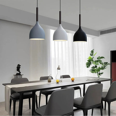 Modern dining room with pendant lights above a long table, showcasing seating for eight and a decorative plant near the window.