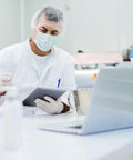 Lab technician using tablet and interacting with laptop in sterile environment