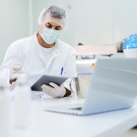 Lab technician using tablet and interacting with laptop in sterile environment