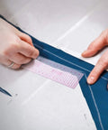 Hands using a pink grid ruler on blue fabric while drafting a sewing pattern with the Top Shelf 13 Piece French Curve Ruler Set For Sewing Pattern Drafting And Fashion Design Includes Hip Curves Tracing Wheels And Measuring Tape Ace Gear To Nail Your Next Creative Project.