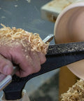 Carbide wood turning tool with red aluminum handle used on a spinning wooden bowl on a lathe