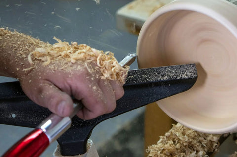 Carbide wood turning tool with red aluminum handle used on a spinning wooden bowl on a lathe