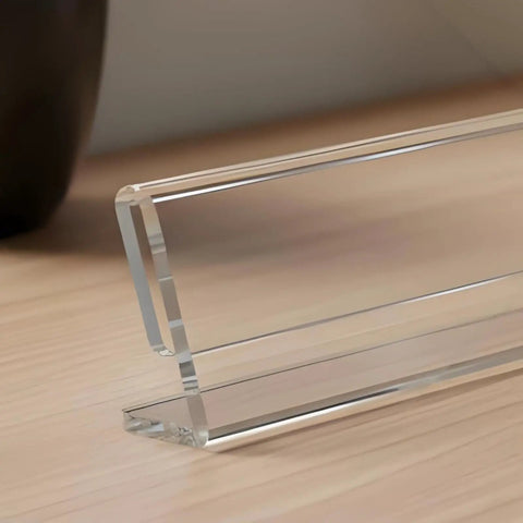 Close-up of a clear acrylic desk name plate with a horizontal slant back, part of a 12 pack 2x8 sign holders, on a wooden table.