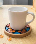 White mug on a wooden coaster with orange and blue mosaic tiles using Mosaic Grout For Crafts Black 400g Quick Dry Crystal Tile Grout.