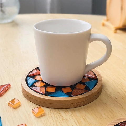 White mug on a wooden coaster with orange and blue mosaic tiles using Mosaic Grout For Crafts Black 400g Quick Dry Crystal Tile Grout.