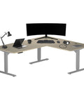 L Shaped Electric Standing Desk Acting As A Game Changer For Your Home Office With Roomy 72 By 60 Inch Corner Layout To Roll Out Multiple Screens And Set Up Shop In Sturdy Gray Frame And Beech Top, featuring a laptop and a monitor.
