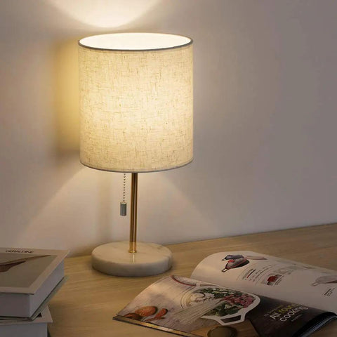 Gold Marble Base Bedside Table Lamp For Bedroom And Office on wooden desk with open book, emitting warm ambient glow.