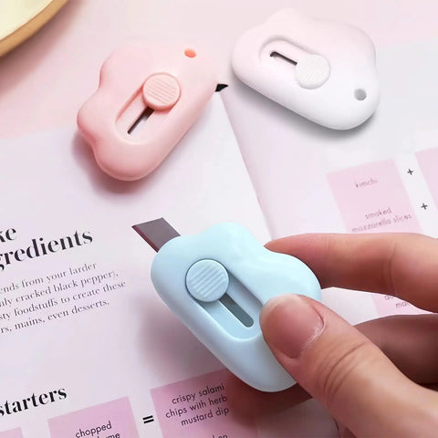 9 Pack Retractable Box Cutter Set With Mini Letter Opener And Cute Cloud Charm in pink, white, and blue on an open book