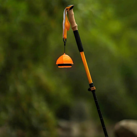 A bright orange 2-In-1 Camping Light And Tent Lantern For Outdoor Adventures, Waterproof Portable Lantern hanging on a trekking pole.