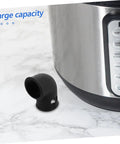 Close-up of a black silicone steam release hose beside a pressure cooker, part of 2 Pack Silicone Steam Release Hoses For Pressure Cooker And Air Fryer, High Temperature Resistant Gasket Tubes, Quick Install No Fuss Setup, Safety Valve Replacement, Keeps Pressure Steady For Juicy Even Cooking Results.