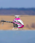 M2 V3 Sport BNF RC Helicopter in flight, pink body with OFS3 Plus Flight Controller, over a scenic outdoor backdrop