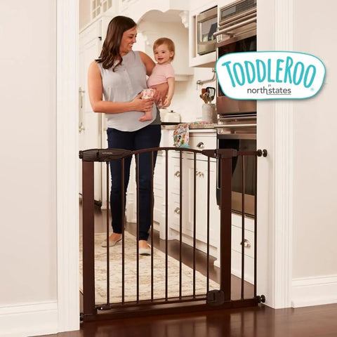 Stone Arch Auto Close Baby Gate For Doorways Bronze Metal Safety Gate in kitchen doorway with parent and child nearby.