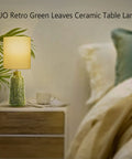 Green Ceramic Table Lamp With Leaf Pattern And White Linen Shade, 17 Inch Tall, on a bedside table