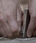 Hands using Waterproof Magnesium Firestarter Kit 2 In 1 with flint serrated striker on rock, showcasing sparks for survival use.