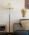 Two Piece Antique Brass Lamp Finials Set For Lamp Shade Nut Screw Cap Metal Knob Topper Decorative Replacement DIY Table Or Floor Light Harp Adapter Kit shown installed on a floor lamp next to a sofa.