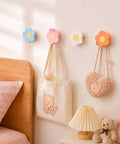 Four Pack Hand Carved Wood Daisy Wall Hooks Decorative Multi Color Coat And Robe Hanger Rack For Bathroom Kitchen Nursery, pink, blue, white, and orange hooks holding bags.