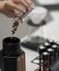 Single Dose Coffee Storage Tubes With One Way Exhaust Valve 8 Piece Set Espresso Dosing Jars And Walnut Holder pouring coffee beans.