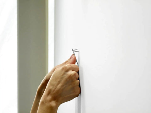 Hands installing a Claw Drywall Picture Hanger Set, Holds 45 Lbs Per Hook, Includes 3 Hooks And 3 Spot Markers, Stainless Steel Silver Finish