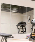 Twelve 12 inch frameless mirror tiles for home gym and garage create custom full length wall reflections with workout equipment visible.